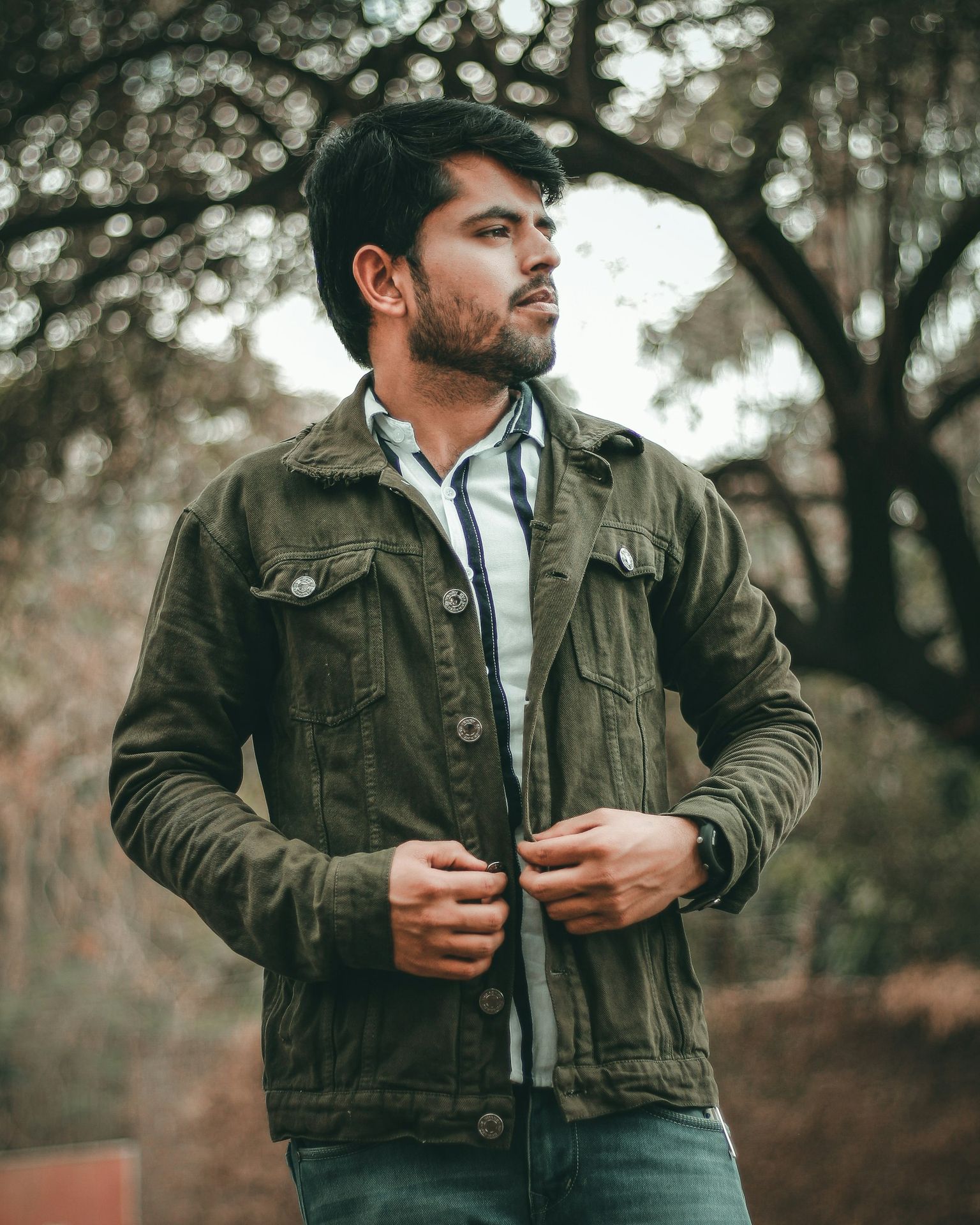 a man standing in front of a tree with his hands in his pockets